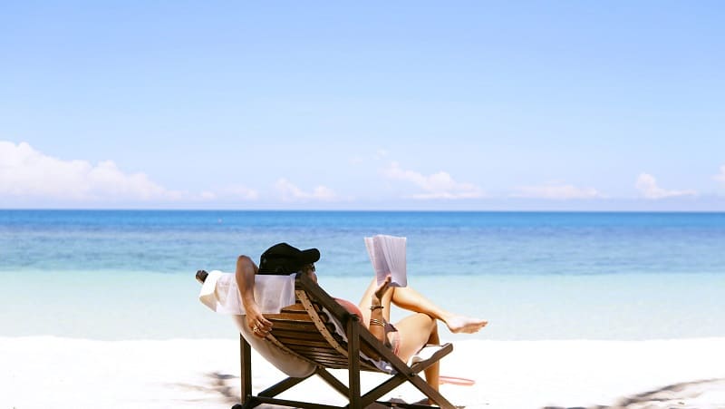 young woman on vacation relaxes by the beach while reading a book