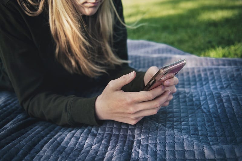 woman uses an app on her smartphone while lying on a blanket at the park