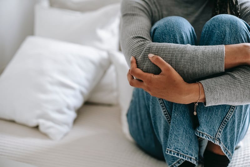 sad woman hugs her knees while sitting on the bed