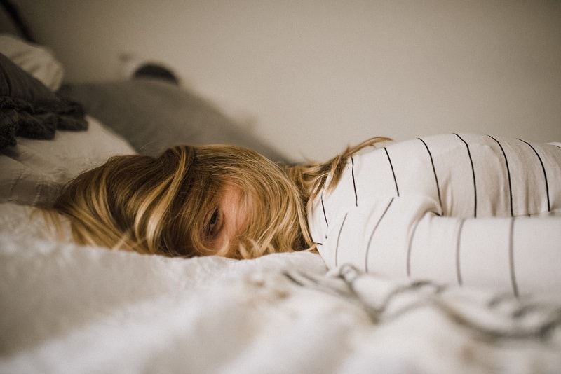 young woman with blonde hair lying in bed and struggling with overcoming perfectionism