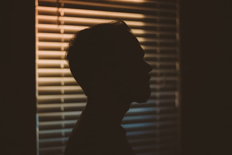 the silhouette of a sad young man in a dark room