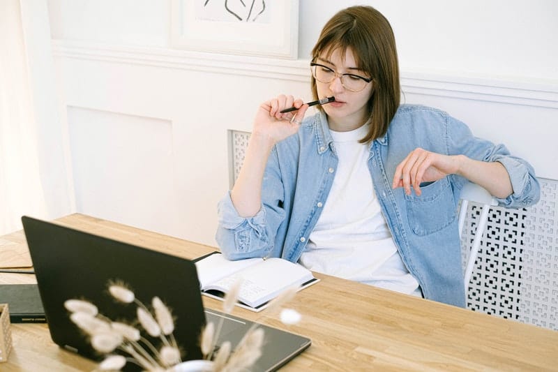 young business woman thinks while working on her laptop at home