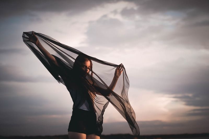 woman standing with a big black scarf as the wind blows