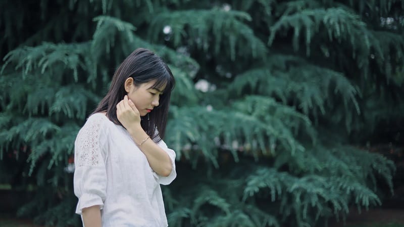 sad young woman with black hair standing in front of trees