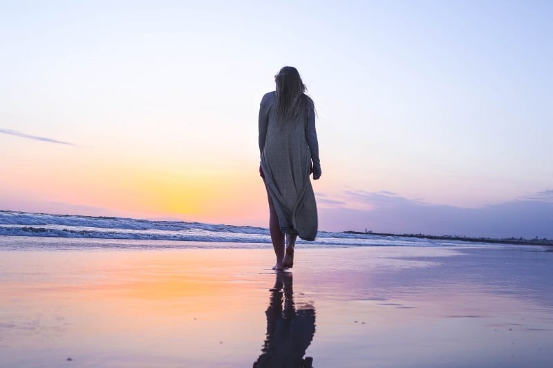 emotionally unavailable woman walking alone on the beach at sunset