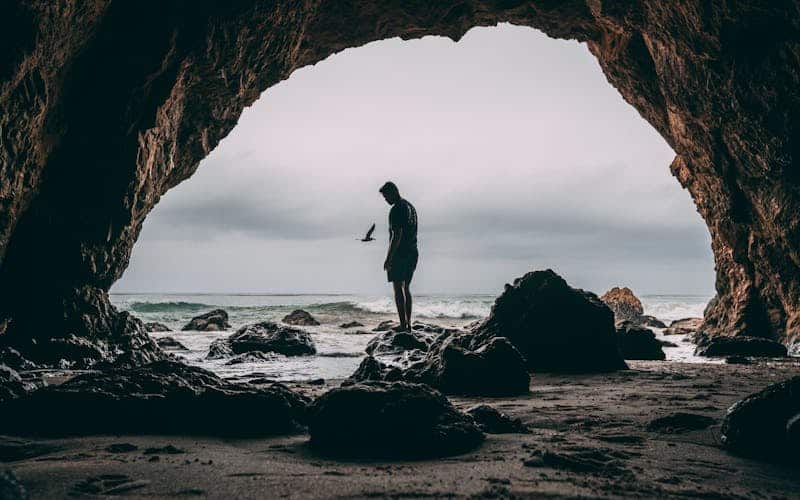 a man stands on a rock in a cave next to the beach