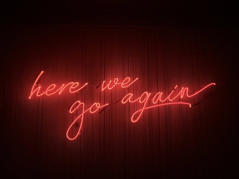 a neon sign that says: here we go again