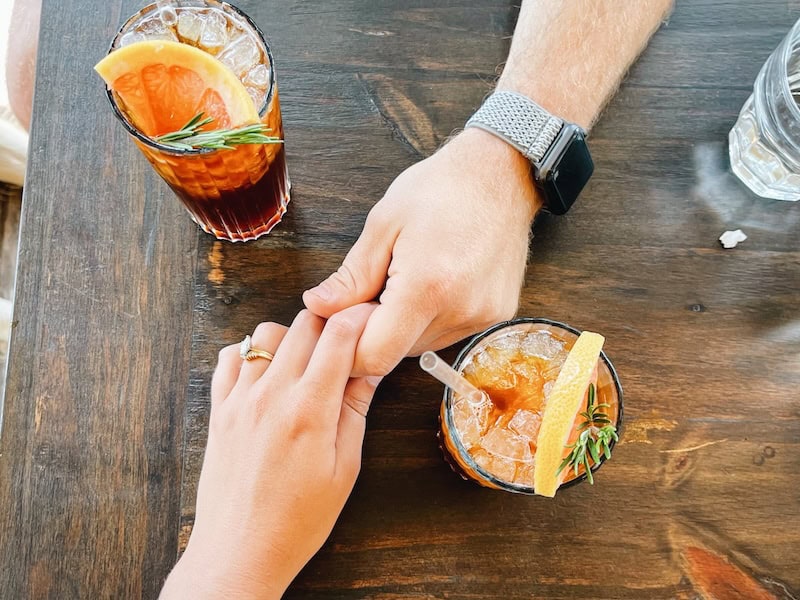 a man and woman hold hands on a table next to two cocktails