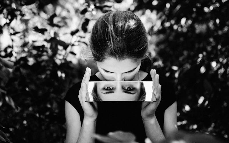 a woman looks down at a mirror and the mirror reflection shows her eyes