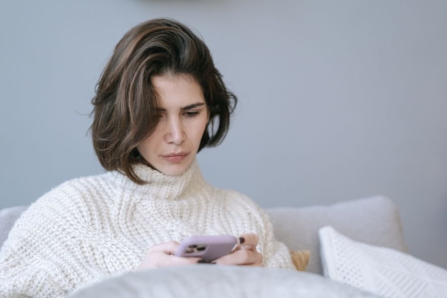 a woman with a sad facial expressions looks at her phone