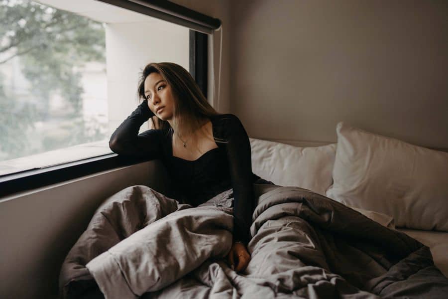 a woman laying in bed and looking out the window